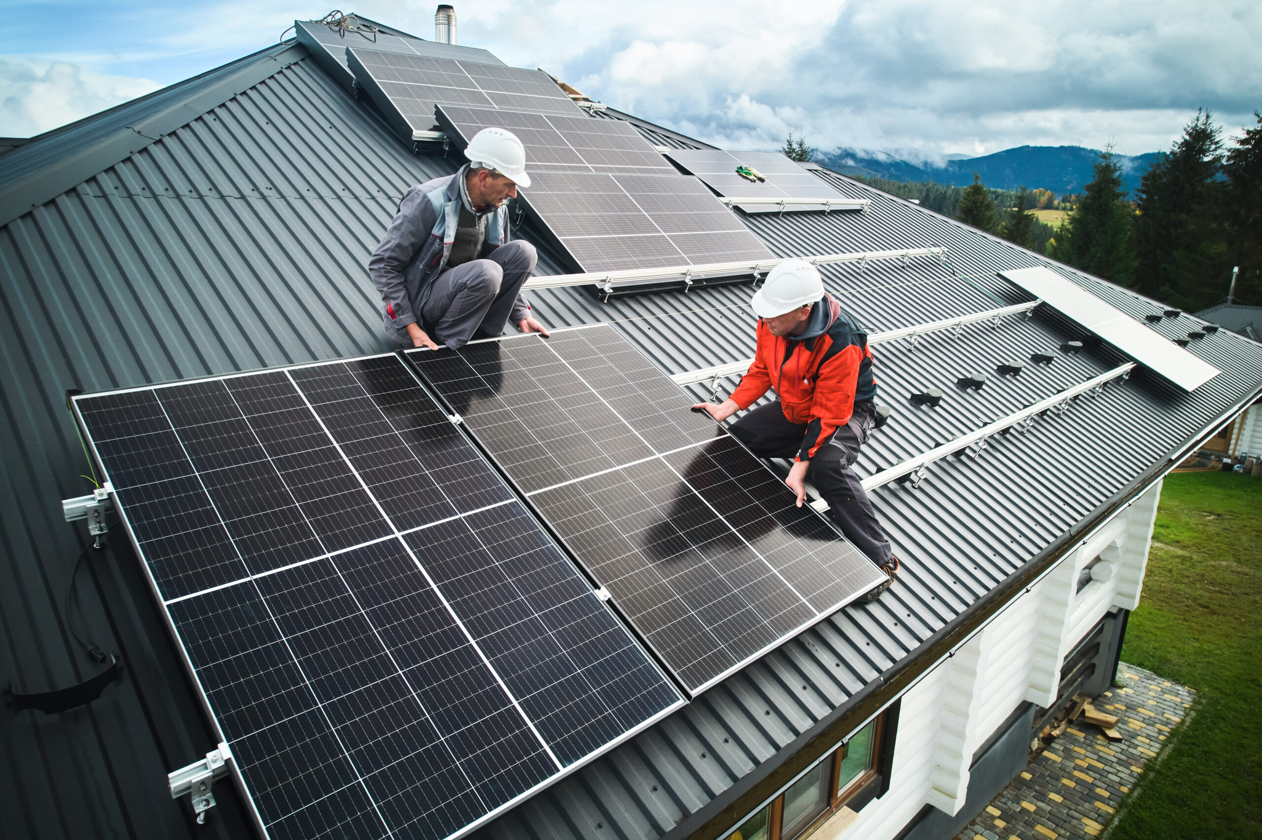 Workers building photovoltaic solar module station on roof of house. Men electricians in helmets installing solar panel system outdoors. Concept of alternative and renewable energy. Aerial view.