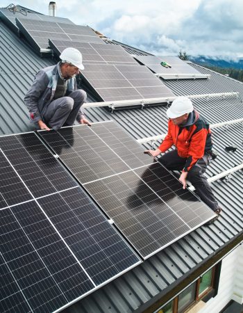 Workers building photovoltaic solar module station on roof of house. Men electricians in helmets installing solar panel system outdoors. Concept of alternative and renewable energy. Aerial view.