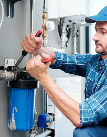 Young plumber or technician in workwear using pliers while installing or repairing system of water filtration